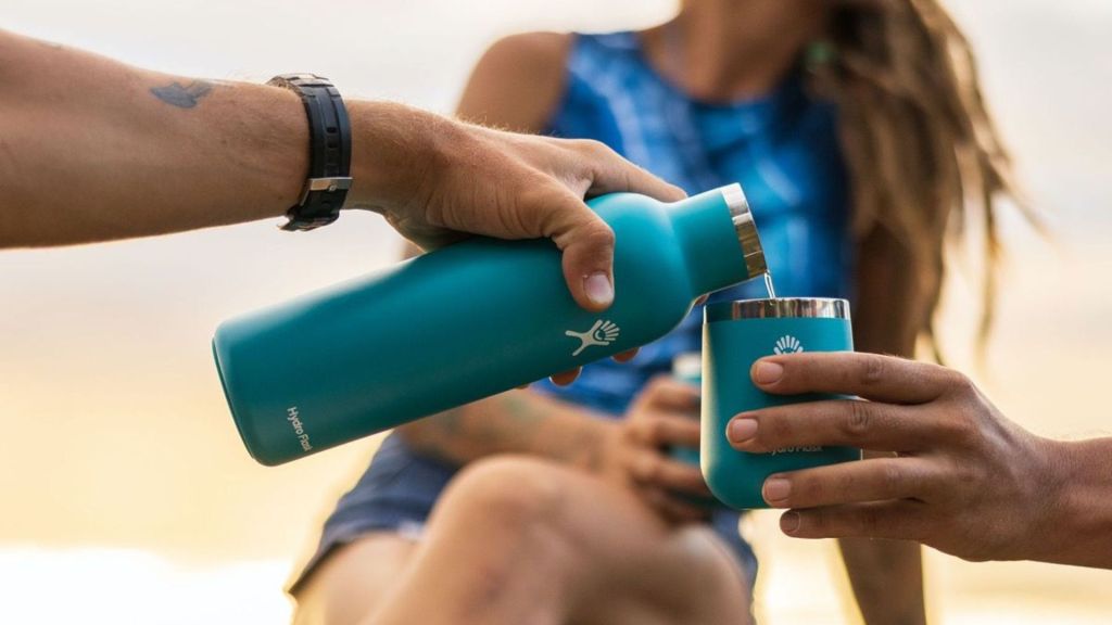 A person pours wine from a turquoise Hydro Flask Bottle into a matching tumbler.